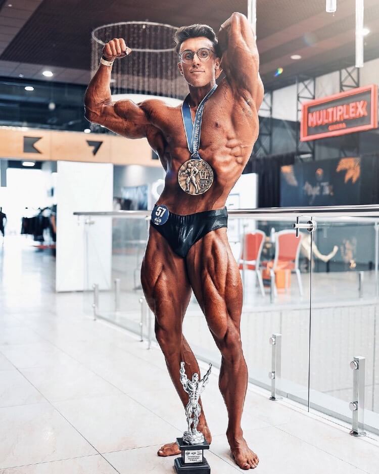 Brandon Harding flexing and showing off his ripped muscles, standing alongside a medal he won after a bodybuilding competition.
