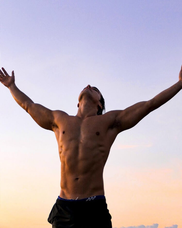 Hans Weiser standing shirtless with his hands spread out wide towards the sky.