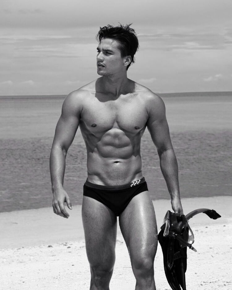 Hans Weiser walking shirtless down the beach in a black and white photo, looking ripped and chiseled.