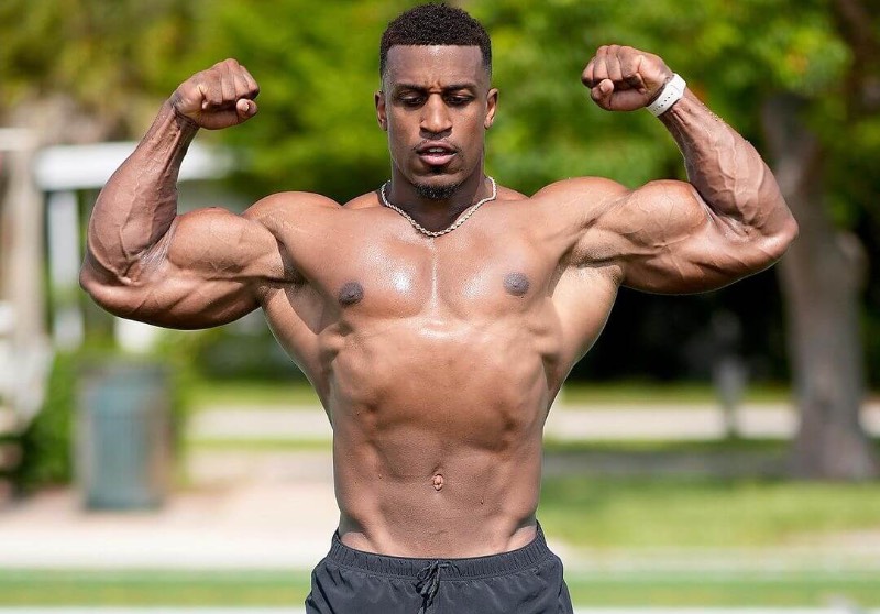 Ashton Hall hitting a shirtless front double biceps pose at front yard